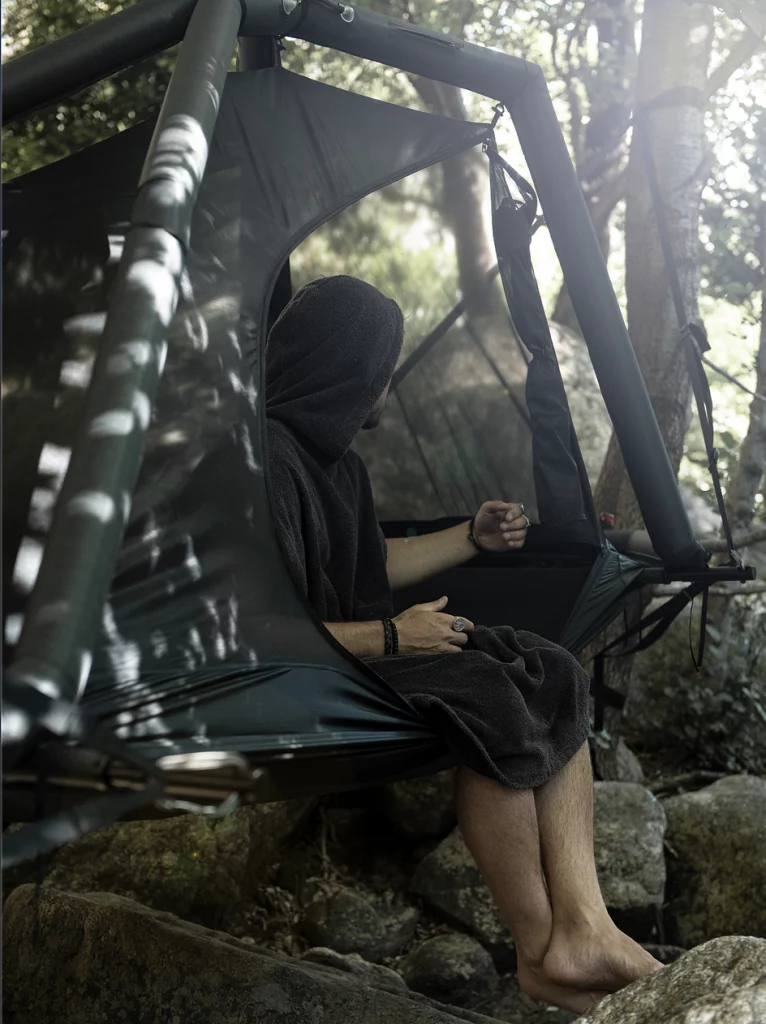 Person sitting in EXOD Monolith Tent suspended between trees in a forest