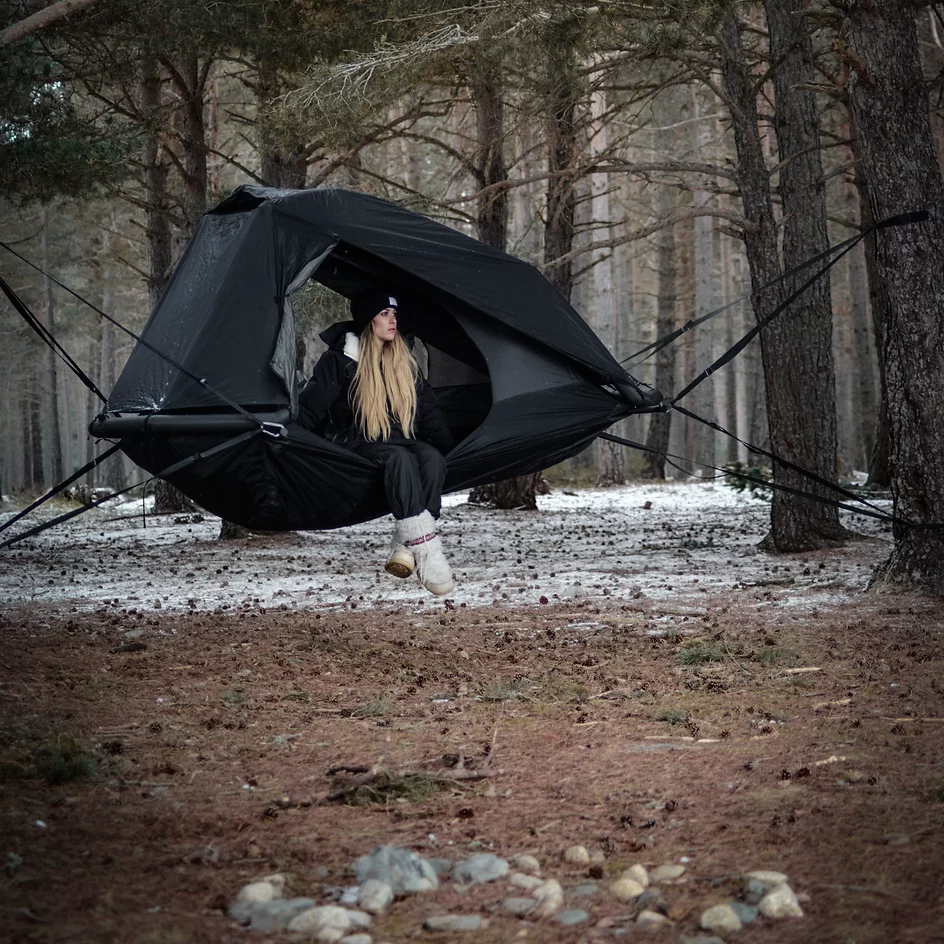 Woman sitting in EXOD Monolith Tent suspended between trees in a forest