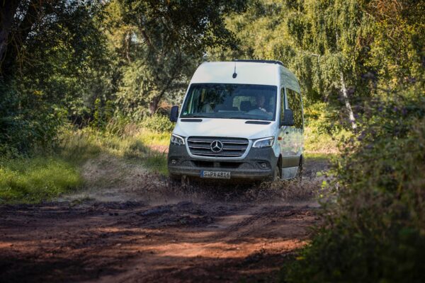 Mercedes-Benz Sprinter driving through a mud puddle on a forest road.