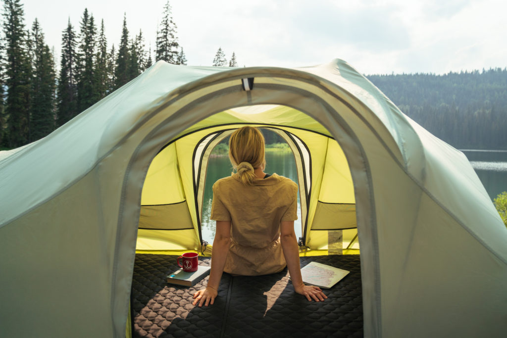 Woman looking out of a Rev Tent at a mountain lake.